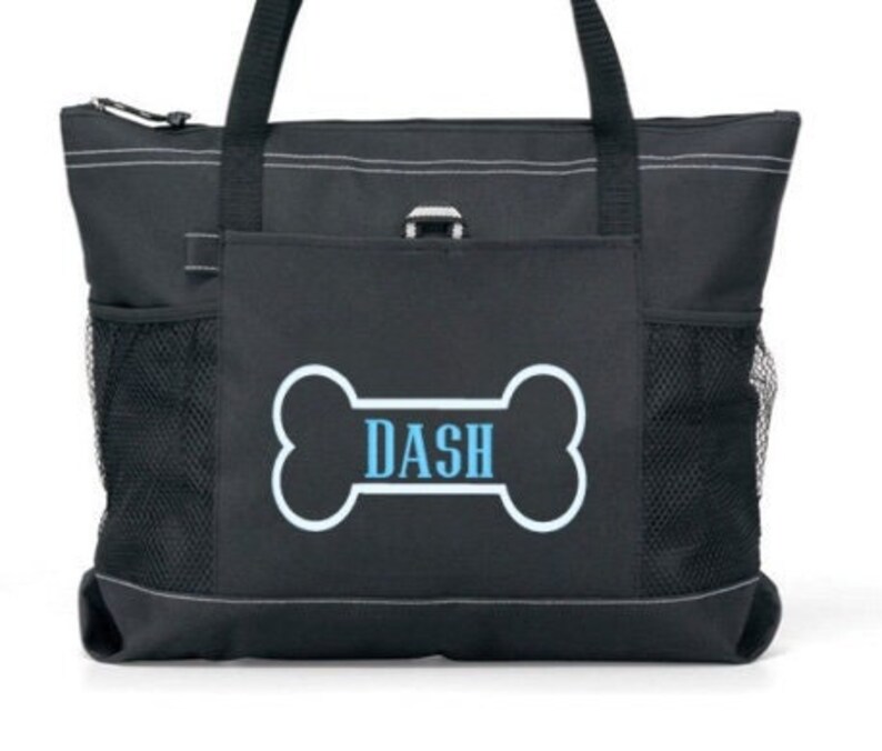 May include: Black tote bag with a white bone-shaped design and the name "DASH" in blue text. The bag has a zipper closure, two side pockets, and a front pocket.