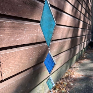 Könnte beinhalten: Ein blauer und grüner Buntglas-Sonnenfänger in Diamantform mit einem Kristall-Tropfen, der unten hängt.