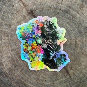 May include: A black and white sticker of a robot wearing a floral crown. The robot has a large, round head with a single eye and a pair of goggles. The floral crown is made of colourful flowers, including pink, blue, yellow, and green.