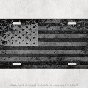 May include: A black and white distressed American flag design on a license plate. The flag is faded and worn, giving it a vintage look.