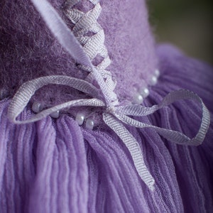 May include: A purple dress with a white lace-up back and a tulle skirt. The dress is decorated with white beads.