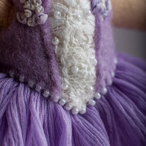May include: A purple knitted doll dress with a white lace bodice and pearl embellishments.