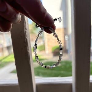 Op de afbeelding: Een armband met afwisselende heldere en zwarte kralen. De armband is gemaakt van kleine, rechthoekige kralen.