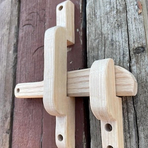 May include: A wooden latch with a simple design, featuring a rectangular shape with a rounded edge and two holes for mounting. The latch is made of light-coloured wood and has a natural finish.