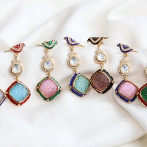 Könnte beinhalten: Ein Set mit sechs Paaren Hängeohrringen mit einem Vogel-Anhänger und einem quadratischen Stein. Die Steine sind mit einem floralen Muster verziert und in Pink, Blau, Grün und Weiß erhältlich. Die Vögel sind in verschiedenen Farben bemalt, darunter Blau, Grün, Rot und Schwarz.