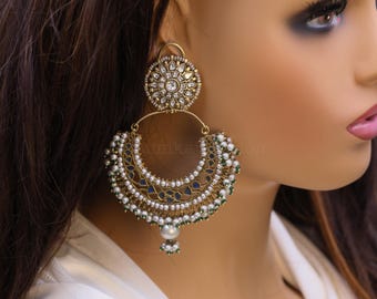 May include: Gold and white statement earrings with a large round pendant and a crescent-shaped dangle with pearl and green accents.