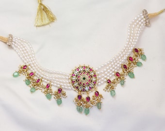 May include: A multi-strand pearl necklace with a large, round pendant featuring pink and green gemstones. The pendant is surrounded by smaller pearls and has a gold setting.