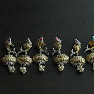 May include: Six pairs of silver and gold fish-shaped earrings with colourful stones. Each earring has a round, textured, gold-coloured pendant with a pearl tassel.