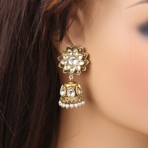 May include: Gold dangle earrings with a floral design and clear stones. The earrings have a small pearl detail at the bottom.
