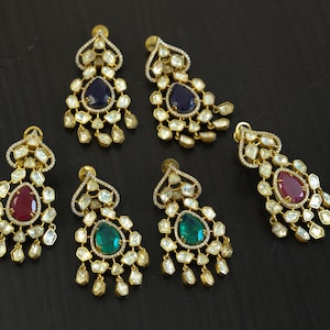 May include: Five pairs of gold dangle earrings with teardrop-shaped gemstones. The earrings feature a variety of colors, including red, blue, and green.