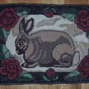May include: A brown and gray rabbit rug with a floral border. The rug is made of wool and has a textured surface. The flowers are red, white, and green.