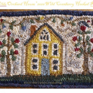 May include: A hooked rug depicting a yellow house with a blue door, surrounded by two trees with red berries. The rug has a dark blue border and is labeled "Olde Orchard House" and "2020 Wild Cranberry Hooked Rugs".
