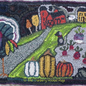 May include: A colorful hooked rug depicting a Thanksgiving scene with a turkey, pumpkins, a house, and a field of vegetables. The rug is made with a variety of colors and textures, including brown, green, orange, and red. The rug is signed "Wild Cranberry Hooked Rugs".