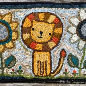 May include: A colorful hooked rug with a brown and yellow lion, a yellow sunflower, and a white flower with a gray center. The rug has a black border and the text "Wild Cranberry Hooked Rugs" is in the bottom right corner.