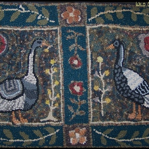 Puede incluir: Una alfombra de ganchillo con fondo azul y dos gansos en el centro. Los gansos son blancos y grises con patas naranjas. La alfombra tiene un borde floral con flores rojas, naranjas y amarillas.