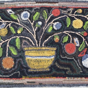 May include: A hooked rug depicting a stylized tree with red, yellow, and blue fruit, green leaves, and small birds. The tree is in a yellow pot with a blue stripe. The rug has a black background and a brown, red, and gray border. The text "Wild Cranberry Hooked Rugs" is in the bottom right corner.
