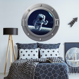 Peut inclure: Un autocollant de hublot rond de couleur argent avec une scène spatiale à l'intérieur. La scène représente un astronaute flottant dans l'espace avec une planète en arrière-plan.