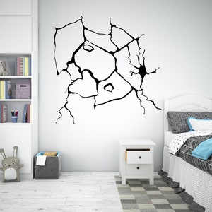 May include: Black and white wall decal of a cracked wall. The decal is applied to a white wall in a room with a white nightstand and a white bed with a blue and white patterned bedspread.