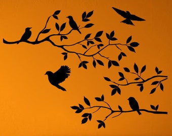 May include: Black silhouette wall decal of a tree branch with birds on an orange wall. The decal is above a white couch with orange throw pillows.