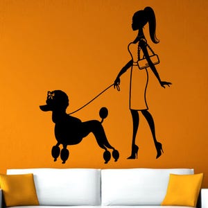 Puede incluir: Pegatina de pared de silueta negra de una mujer paseando a un caniche. La mujer lleva un vestido y un bolso. El caniche está con una correa.
