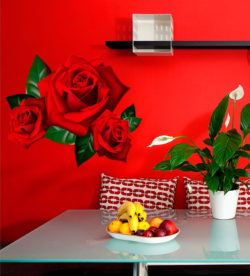 Puede incluir: Una pared roja con un estante y una caja blanca en &eacute;l. Hay tres rosas rojas en la pared. Una planta en maceta con flores blancas est&aacute; en el lado derecho de la imagen. Una mesa de vidrio con un taz&oacute;n de fruta est&aacute; en primer plano.