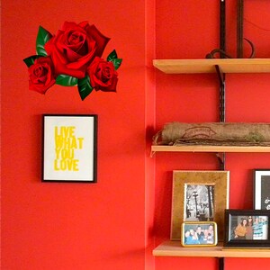 Puede incluir: Una pared roja con una impresi&oacute;n enmarcada que dice "Live What You Love" y una pegatina de rosa roja en la pared. Hay estantes de madera con un saco de arpillera en el estante superior y fotos enmarcadas en el estante inferior.