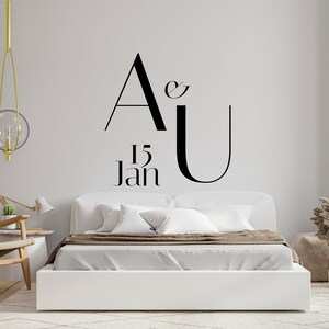 May include: A white bed with a brown blanket and white pillows in a room with a gold light fixture and a plant in a vase. The wall behind the bed has a black and white graphic that says "A & U 15 Jan".