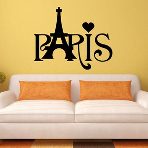 May include: A white sofa with two orange cushions in front of a yellow wall with a black vinyl decal of the Eiffel Tower and the word "PARIS" with a heart above the "I".