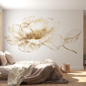 Op de afbeelding: Een grote bloemenmuursticker in beige en goudtinten. Het ontwerp toont een gedetailleerde pioenroos met delicate bloemblaadjes en een stengel, wat een verfijnd en artistiek accent creëert voor het interieur.