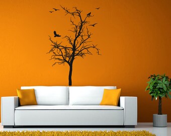 May include: A white couch with yellow throw pillows sits in front of an orange wall with a black silhouette of a bare tree with birds on it. A potted green plant is on the right side of the image.