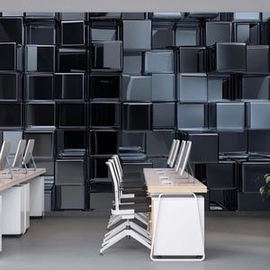 May include: Modern office space featuring desks with computer monitors and chairs. The backdrop is a textured wall of dark, reflective cubes. A potted plant adds a touch of greenery. The room has a minimalist design with a polished concrete floor.