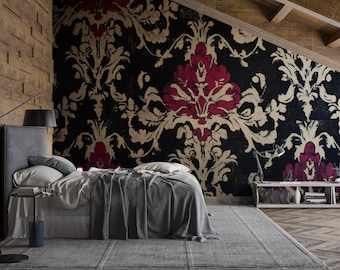 May include: A bedroom featuring a bed with gray bedding, a patterned rug, and a statement wall with a black, red, and gold damask design. A wooden accent wall and a side table with a lamp complete the space.