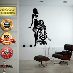 May include: A black silhouette of a woman in a dress with floral and swirl designs. The wall decal is on a white wall. The image also includes a chair, ottoman, and a small table with a lamp.