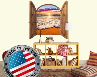 Op de afbeelding: Een decoratieve muursticker met een gebogen raam met open houten luiken die een strandscene met zonsondergang en schuimige golven onthullen. De sticker is gemaakt in de VS en heeft de tekst "Made in the USA American Product".