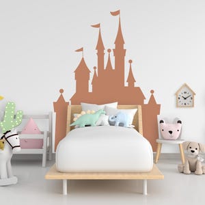 May include: A child's bedroom featuring a brown castle wall decal above a bed with white bedding. The room includes a rocking horse, a cactus pillow, and a clock. Decorative pillows shaped like dinosaurs and a bear are on the bed.