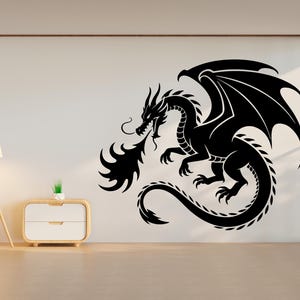 Könnte beinhalten: Schwarzer Drachen-Wandtattoo. Der Drache wird mit ausgebreiteten Flügeln dargestellt, die Feuer speien. Der Drache ist eine Silhouette mit komplizierten Details. Das Tattoo ist an einer weißen Wand angebracht.