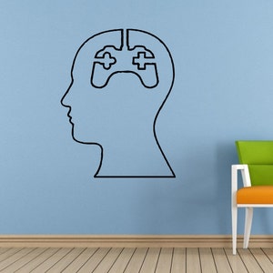 Puede incluir: Un contorno en blanco y negro de una cabeza humana con un mando de videojuego dentro de la cabeza. La cabeza está en una pared azul claro. Una silla verde y naranja está en primer plano.