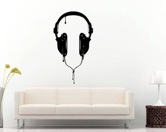 May include: Black wall art featuring a stylized headphone design with a dripping paint effect. The headphones are centered on a white wall, creating a modern and artistic statement. The design includes the earcups, headband, and connecting wire.