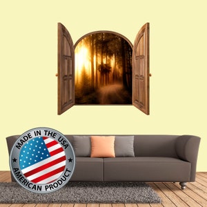May include: A wall decal featuring a wooden door opening to reveal a scenic view of a sunlit forest path. The decal is shown on a wall with a brown couch and a gray rug.