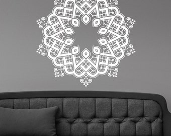 May include: White, ornate mandala wall decal with a symmetrical design. The decal is affixed to a gray wall above a gray sofa with a matching pillow. The mandala features geometric shapes and floral accents.
