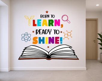 May include: A wall decal with the words "Born to Learn, Ready to Shine!" in colorful letters. The design includes an open book, a magnifying glass, and science-themed illustrations. The decal is applied to a white wall in a room with a door and a potted plant.