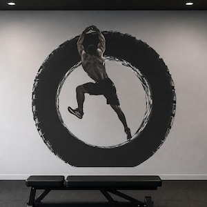 May include: A black and white mural of a person jumping through a tire, set in a gym. The gym has black weights, a bench, and a weight rack. The mural is the focal point of the room.
