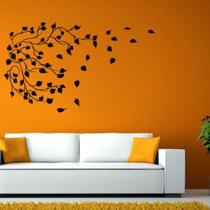 Könnte beinhalten: Ein weißes Sofa mit orangen Kissen steht vor einer orangen Wand mit einer schwarzen Silhouette eines belaubten Zweigs mit Blättern, die im Wind wehen.