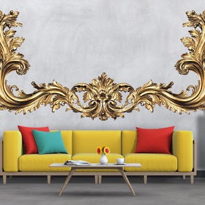 May include: A gold-coloured, ornate wall decor piece above a yellow sofa with red and teal cushions. The wall is light grey. A small white table and a wooden cabinet are also in the room. A plant is on the left.