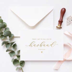 Personalized wedding day card reading “Today I Get to Call You My Husband” in gold foil with custom wedding date, modern minimalist bride to groom wedding card styled flat lay with envelope, ribbon, and eucalyptus.
