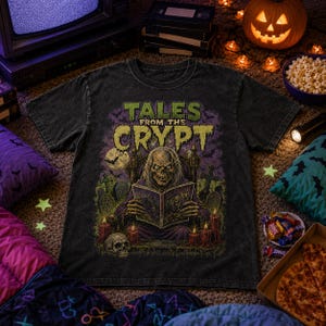 May include: A black acid-wash t-shirt featuring a graphic print of the Crypt Keeper from Tales from the Crypt reading a book in a graveyard. The design includes green text, a full moon, tombstones, a skull, and red candles on a dark background.