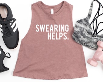 May include: A mauve tank top with the text "SWEARING HELPS." in white. The tank top is paired with a black and gray sports bra, pink dumbbells, and black sneakers.