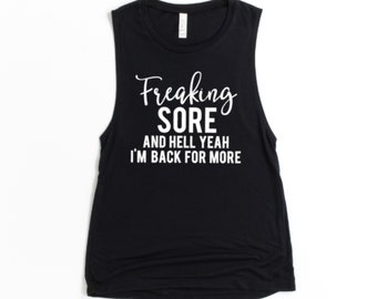 May include: Black sleeveless workout tank top with white text that reads "Freaking Sore and Hell Yeah I'm Back For More". The tank top is made of a soft material and is perfect for the gym or casual wear.