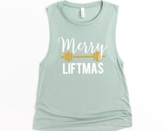 May include: A sleeveless, light green muscle tank top with the words "Merry LIFTmas" in white script and a gold barbell graphic. The shirt is made of a soft material and is suitable for workouts or casual wear.