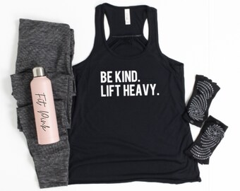 May include: Black tank top with the text "BE KIND. LIFT HEAVY." in white.  The tank top is paired with gray leggings, a pink water bottle with the text "Fit Pink" and black fingerless gloves with white dots.